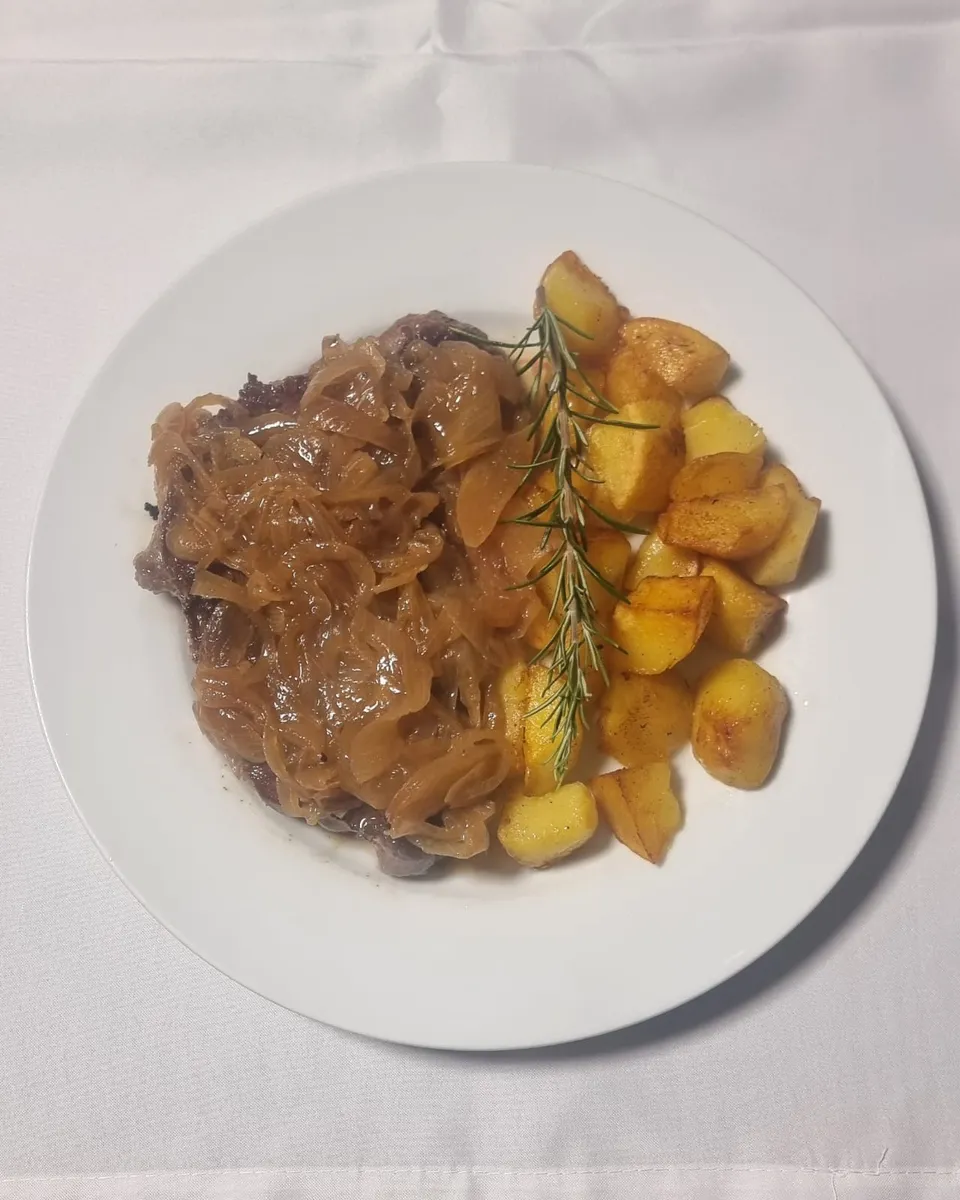Pork goulash with onions and fried potatoes, garnished with rosemary