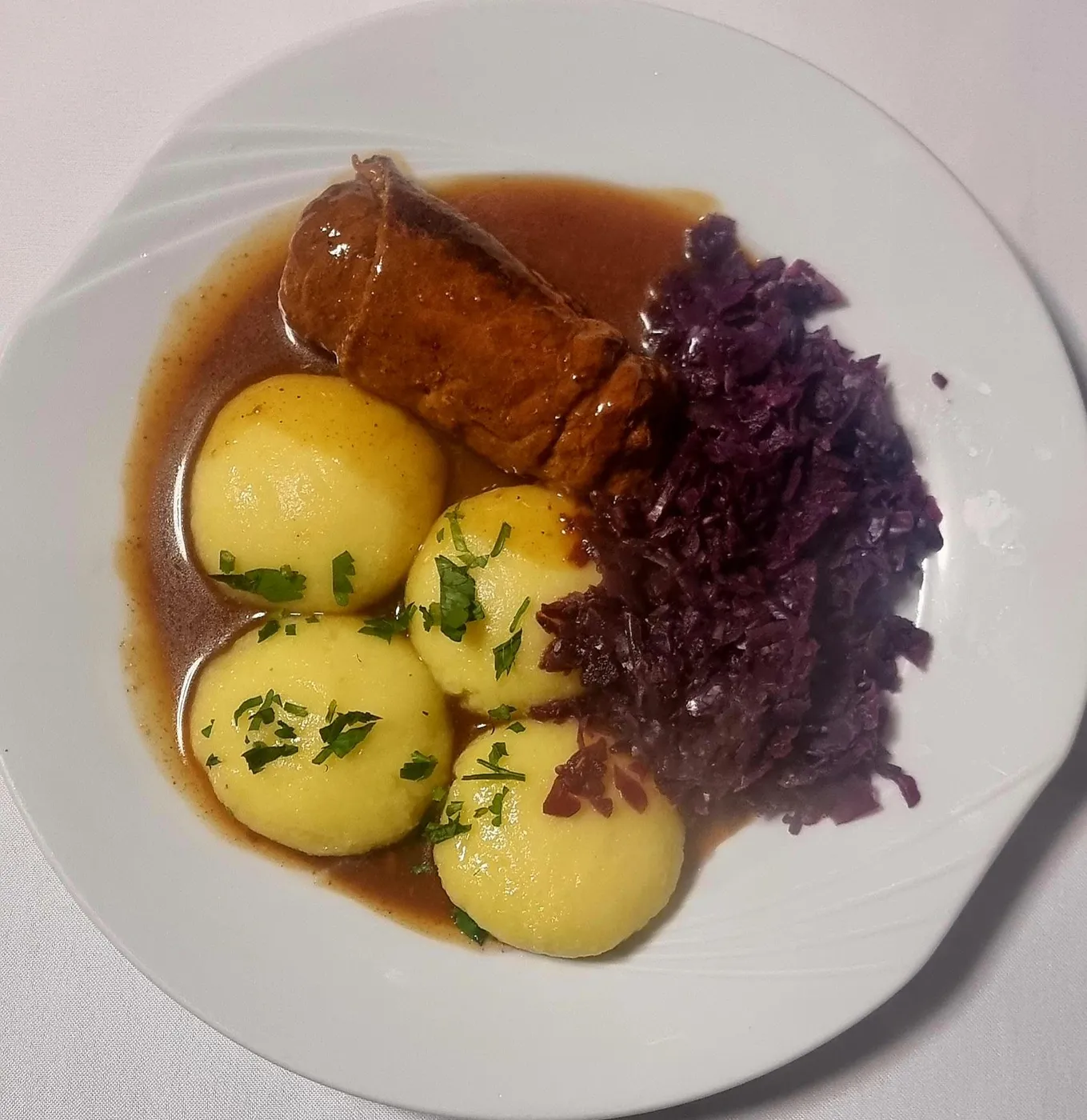 Beef roulade with two potato dumplings, red cabbage and dark gravy on a white plate